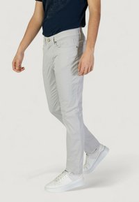 Pantalones ajustados de color gris claro hechos de algodón, con cierre de botón, bolsillos frontales y detalles de costura sutiles, combinados con zapatillas blancas.
