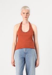 Débardeur couleur rouille avec un col dégagé, orné de clous métalliques le long de l'encolure. Le tissu est lisse, associé à un jean bleu clair.