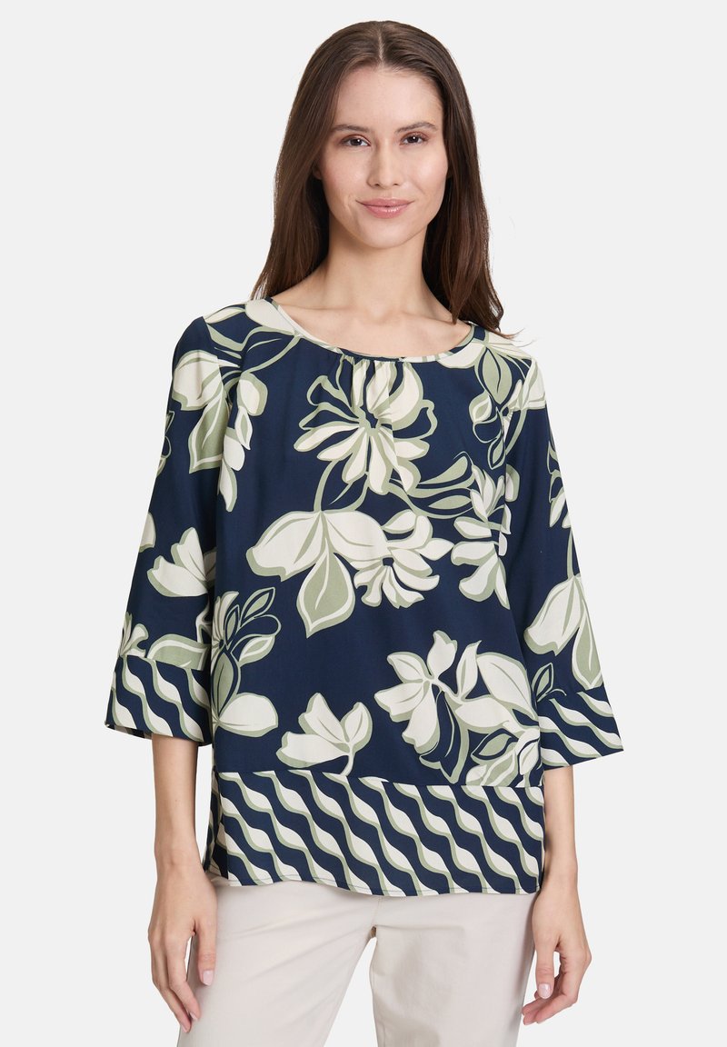 Granatowa bluzka w kwiaty z zielonymi i białymi wzorami, z okrągłym dekoltem i rękawami o długości trzech czwartych, wykonana z lekkiego materiału.