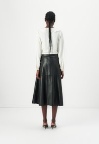 Schwarze Leder-Midi-Rock mit ausgestelltem Design, ausgestattet mit einem verdeckten Reißverschluss und glatter Textur, kombiniert mit einer weißen Bluse.