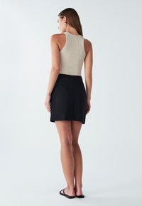 Top corto aderente beige a costine abbinato a una minigonna nera a vita alta, con una texture liscia e una chiusura a zip discreta sul retro.