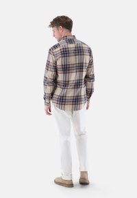 Beige kariertes Flanellhemd mit Navy- und Brauntönen, langen Ärmeln, Knopfmanschetten und abgerundetem Saum, kombiniert mit weißen Hosen.