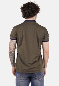 Polo shirt verde oliva a maniche corte, con dettagli in blu navy sul colletto e una texture liscia. Indossato con jeans di denim. Vista da dietro.