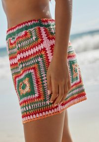 Hæklede, flerfarvede miniskirt med grønne, røde, pink og orange mønstre, prydet med dekorative bølgede kanter og en struktureret finish.