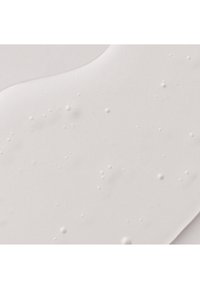 Étale liquide crémeuse blanche et lisse avec de petites bulles et des bords irréguliers sur une surface plane.