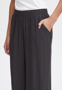 Svarta, lätta, strukturerade byxor med elastisk midja och sidofickor, med en avslappnad passform och något skrynklig tyg.