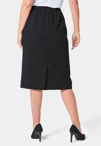 Schwarzer knielanger Rock mit einem elastischen Bund und einem Schlitz hinten, ausgestattet mit einer glatten Textur und einfachem Design. Getragen mit schwarzen High Heels.