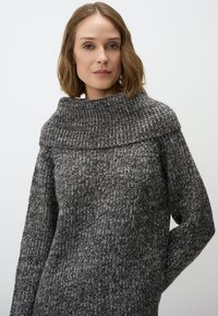 Pull en tricot aux nuances variées de gris, doté d'un col haut et large et de manches longues avec une coupe ample et un motif texturé.