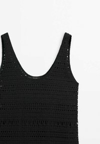 Haut sans manches en tricot crocheté noir avec encolure dégagée présenté sur un fond blanc.