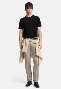 Svart kortärmad t-shirt, beige byxor och en ljusbeige skjorta knuten i midjan. Svart bälte och ankelhöga svarta stövlar.