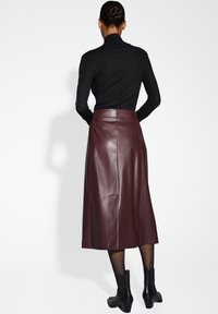 Burgunderfarbene Leder-Midi-Rock mit glatter Textur, hohem Bund und dezenten Seitennähten, kombiniert mit einem schwarzen Rollkragenpullover und Ankle Boots.