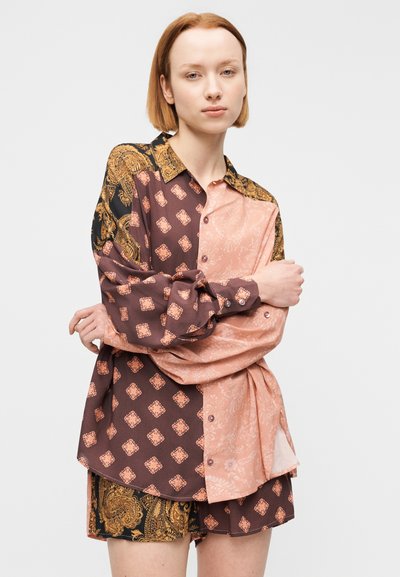 Πουκάμισο με κουμπιά, που συνδυάζει καφέ και ανοιχτό ροζ ύφασμα με περίπλοκα μοτίβα. Μακριά μανίκια, γιακάς με χρυσές λεπτομέρειες και άνετη εφαρμογή.