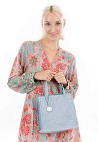 Light blue leather tote bag with short handles, square shape, and a subtle texture. Includes a silver accent tag with logo.