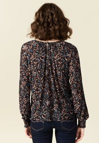 Blusa a fantasia floreale nera, caratterizzata da morbide pieghe, maniche lunghe, polsini elasticizzati e un dettaglio a chiave sul retro del collo.