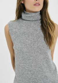 Pulover gri fără mâneci, cu guler înalt, fabricat dintr-un material moale, având un guler ajustat și un design simplu, minimalist.