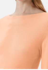 Pull tricot pêche clair avec un col rond, des bordures côtelées et une texture lisse, avec des détails sur les coutures latérales pour un ajustement amélioré.