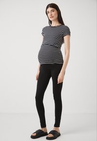 Top per maternità a righe bianco e nero abbinato a leggings neri e sandali neri scivolati. Il top presenta un design aderente e maniche corte.