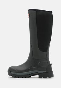 Mustat, vedenpitävät polvipituiset kumisaappaat, joissa on teksturoitu pinta, vahvistettu kärki ja paksu ulkopohja pidon parantamiseksi. Varusteena on neopreenista valmistettu yläosa.