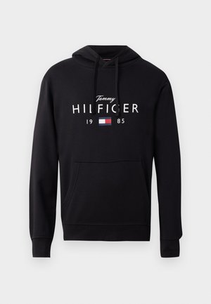 Felpa nera con cappuccio in tessuto morbido, dotata di una tasca frontale, cappuccio regolabile e testo bianco "Tommy HILFIGER 1985" con un piccolo logo aggiuntivo.