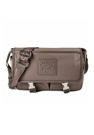 Sac bandoulière marron Lacoste avec sangle réglable, rabat avant, boucles argentées et écusson embossé avec le logo "Lacoste Paris."