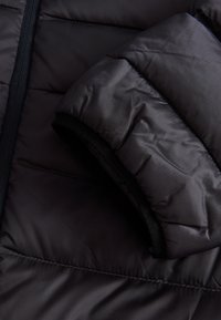 Svart puffjacka ärm, med kvarsömmad textur, slät yttermaterial och en mjuk, elastisk inre mudd för extra komfort.