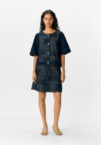 Denimklänning för kvinnor med kortärmad topp och knappstängning samt mönstrad kjol. Mörkblå färg med kontrasterande vita mönster.