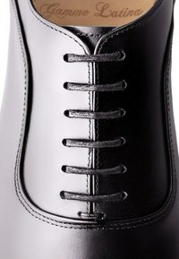 Chaussure en cuir noir avec un design à lacets fermés, comportant six œillets et des lacets plats. Texture lisse et détail de couture subtil.