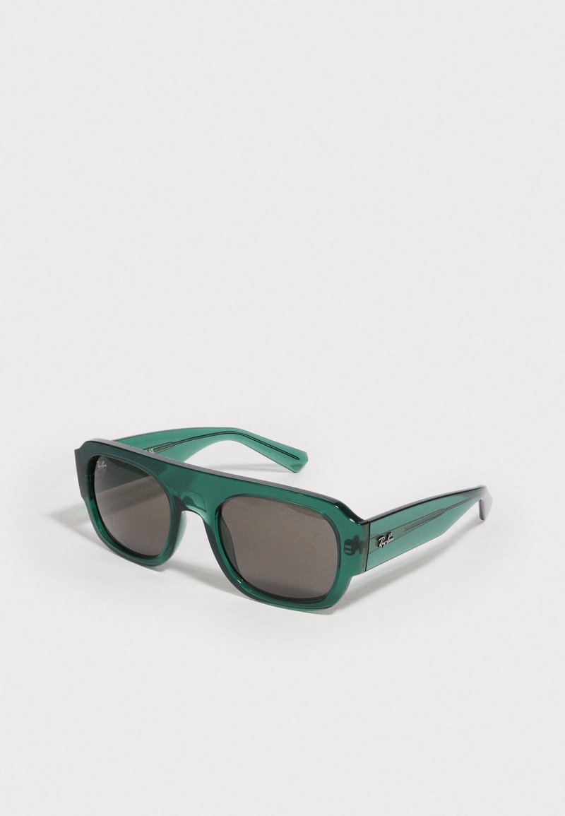 Óculos de sol de plástico verde com uma armação quadrada, lentes escuras e uma discreta marca Ray-Ban na lateral. Textura suave e design arrojado.