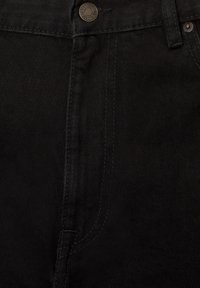 Jean en denim noir en gros plan montrant les détails du bouton et des coutures de poche.