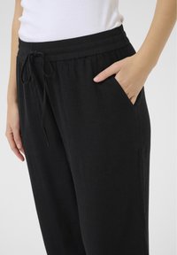 Pantalon noir ample avec taille élastique et cordon de serrage. Doté de poches latérales et d'une texture lisse et douce.
