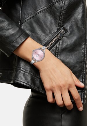Sølv wristwatch med en pink urskive, krystal accenter, og en grå rem, vist på en hånd mod en sort læderjakke.