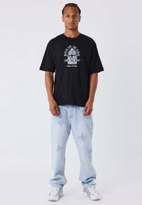 Camiseta negra de gran tamaño con estampado gráfico; jeans de mezclilla azul claro con bordado en forma de estrella; zapatillas blancas con acentos grises.