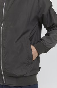 Water-resistant bomber jacket in dark gray. Features a front zipper, ribbed cuffs, and side pockets. Smooth texture and straight silhouette.