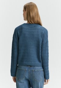 Maglione blu lavorato a maglia con un motivo testurizzato, scollatura a girocollo e orlo a costine. Abbinato a jeans di jeans a vita alta, che mostrano un look casual.