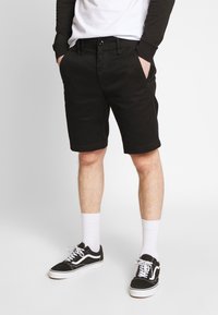 Zwarte katoenen shorts met rechte snit, zijzakken en een tailleband met knoopsluiting, gecombineerd met witte sokken en zwarte sneakers.