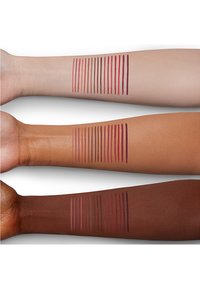 Tre braccia di diverse tonalità di pelle mostrano campioni di rossetto in varie sfumature di rosso e rosa, con linee orizzontali di colore applicato.