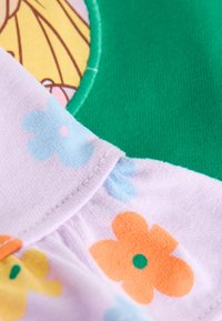 Primer plano de tela con patrones florales coloridos y secciones verdes y amarillas cosidas sobre un fondo suave y púrpura claro.