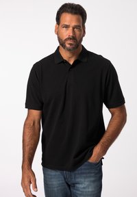 Černé polo tričko s krátkým rukávem, klasickým límečkem, tříknoflíkovou légou a měkkou bavlněnou tkaninou. Model má na sobě modré džíny.