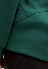 Felpa verde con una finitura testurizzata, caratterizzata da una superficie a coste e una vestibilità leggermente ampia, abbinata a pantaloni neri.