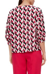 Blouse à manches longues avec un motif zigzag coloré en rose, noir et blanc, à coupe décontractée et avec des poignets froncés.