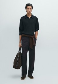 Svart tröja, brunt bälte knutet runt midjan, mörka byxor, bär en mörkbrun mockaväska och bruna skor med snörning.