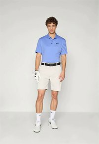 Gaiši zils polo krekls ar apkakli, bēši šorti un balti sporta apavi. Aksesuāros ietilpst melna josta un balta golfa cimdi.