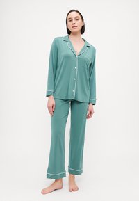 A teal pajama set featuring a button-up long sleeve top with a chest pocket and white piping, paired with matching long pants.