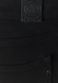 Μαύρος τενεκεδένιος καμβάς με υφή στην επιφάνεια. Διαθέτει δερμάτινο ετικέτα με κυκλικό λογότυπο και μια μικρή τσέπη με επωνυμία.