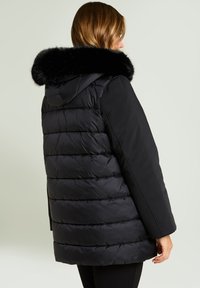 Sort dunjakke med en aftagelig sort kunstpelskrave, der har et quiltet design og en afslappet pasform, vist bagfra.