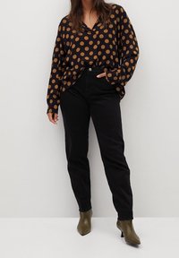 Musta pilkkupaita, jossa on suuria khakiympyröitä, V-pääkappale ja pitkät hihat, yhdistetty mustiin housuihin ja oliivinvihreisiin teräväkärkisiin saappaisiin.