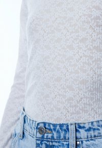 Witte lange mouw top met een textuur van bloemenpatroon, gecombineerd met lichtblauwe high-waisted denim jeans met een zilveren knoop en gestikte naden.