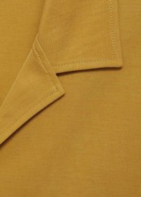 Textured, mustard-colored fabric corner with visible stitching and a sharp pointed fold. Smooth, durable weave with a matte finish.