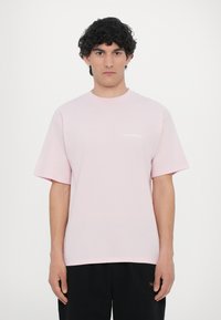 Helles rosa Baumwoll-T-Shirt mit kurzen Ärmeln, Rundhalsausschnitt und einem kleinen weißen "No Problemo"-Textlogo auf der Brust.