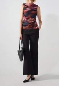 Débardeur multicolore avec une texture froncée, associé à un pantalon large noir et des talons noirs. Le modèle tient un sac à main noir.